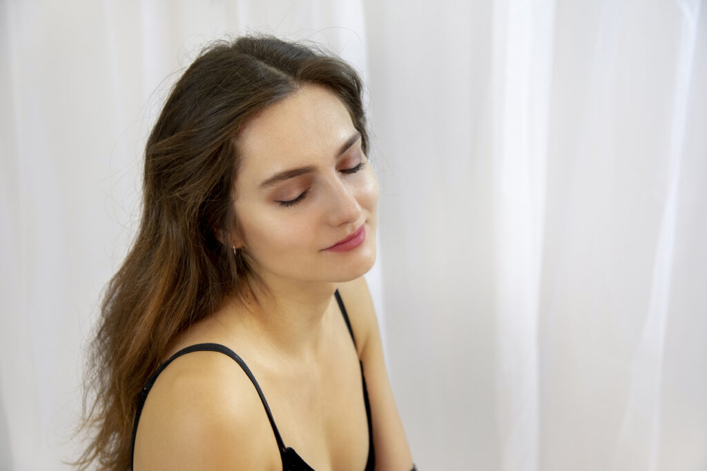 Young woman with healthy skin standing in front of a white curtain