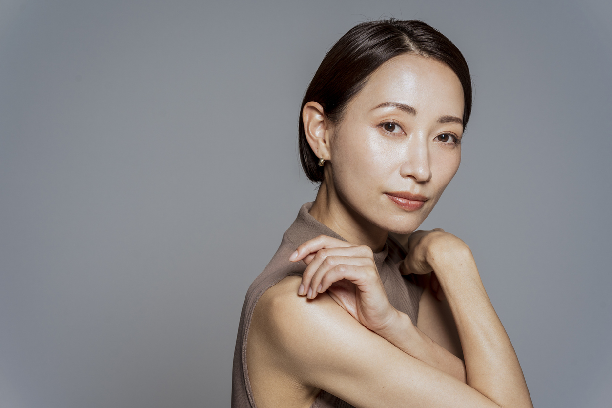 Japanese woman with a bob haircut gently hugging herself, representing confidence and natural rejuvenation associated with Radiesse filler treatments.